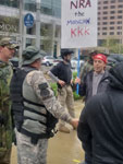 Protestor holding KKK sign surrounded by armed open carry AR-15 at NRA convention 2019 Indianapolis, Indiana